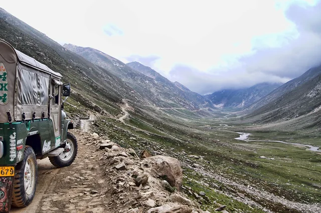 A green jeep on a narrow mountain track above a misty valley